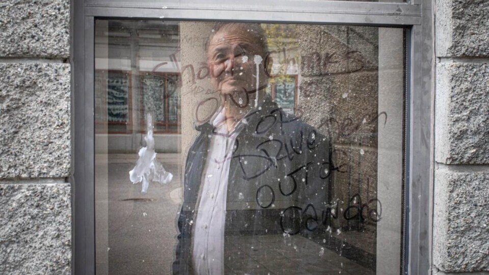 Un homme regarde par la fenêtre, sur laquelle des phrases sont tracées au crayon-feutre.