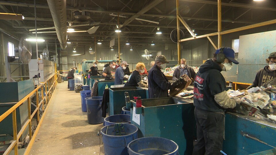 Des employés d'un centre de tri travaillent sur une chaine de travail pour faire le tri des différentes matières recyclables.