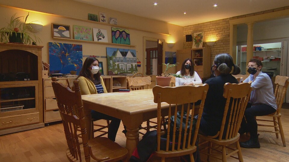 Quatre femmes assises autour d'une grande table, dans une pièce lumineuse, portant des masques.