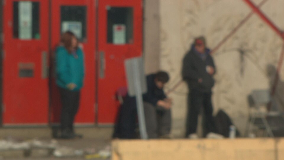 Trois sans-abri logés à Guertin devant les portes de l'aréna. La photo est volontairement hors focus.