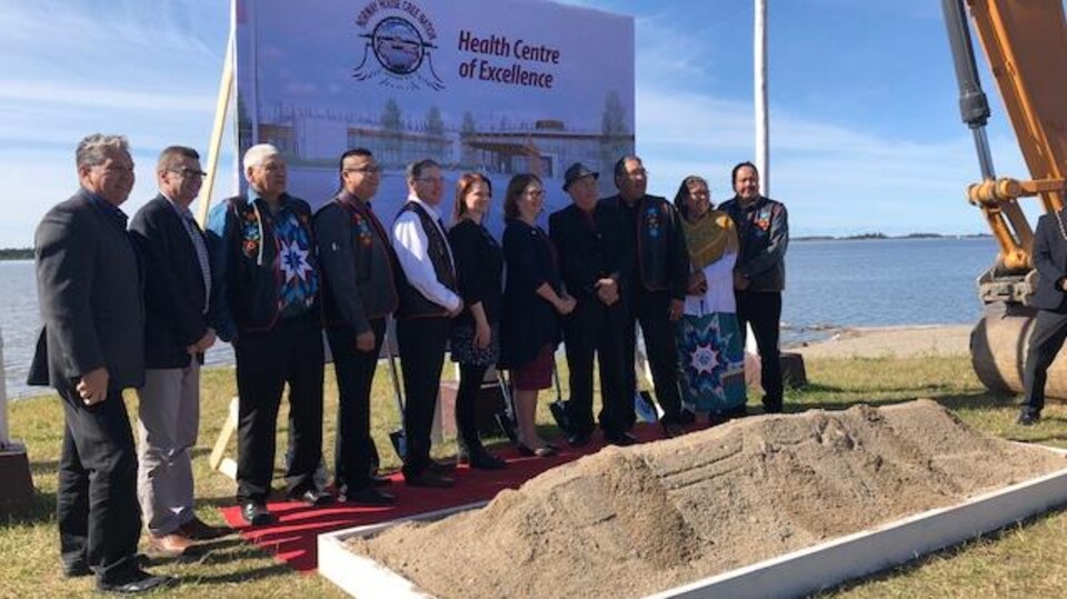 Plusieurs politiciens et leaders autochtones posent devant un bac de terre et près d'un grand panneau qui annonce le « centre d'excellence en santé de Norway House ».