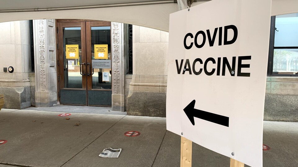 Un panneau indique la direction pour la vaccination contre la COVID-19 devant un bâtiment.