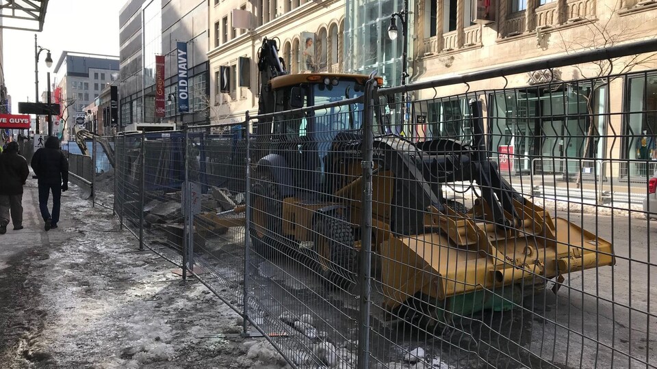 Une clôture empêche la circulation rue Sainte-Catherine, au centre-ville de Montréal, et de la machinerie lourde est stationnée devant les magasins.