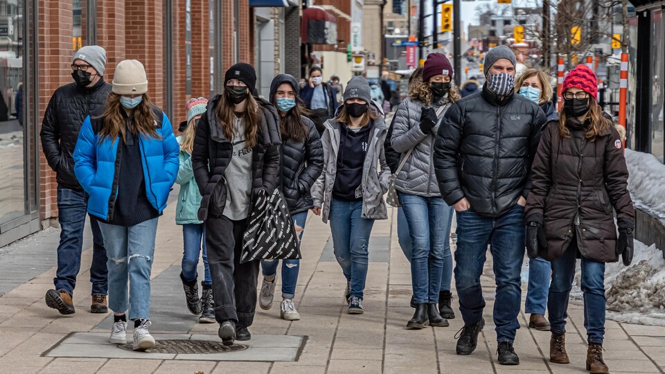 Des gens protégés par un couvre-visage marchent sur le trottoir.