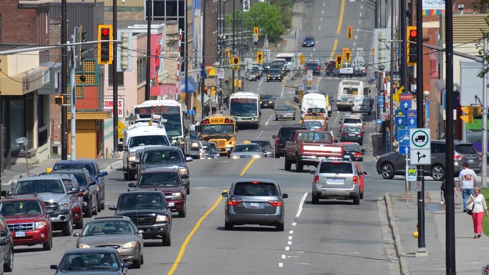 Des véhicules à la file sur une artère achalandée. Il y a des autobus, des camionnettes, des voiture et un taxi.
