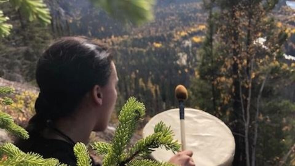 Une personne joue du tambour assise dans la forêt.