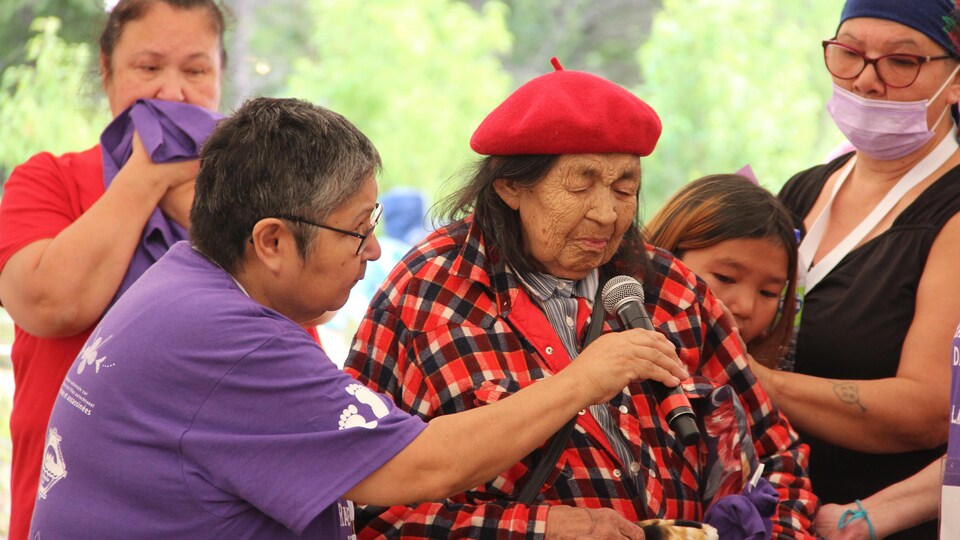 Une femme âgée parle dans un micro, entourée d'autres femmes.