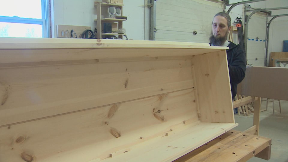 Un homme barbu tenant entre ses mains un cercueil en bois.