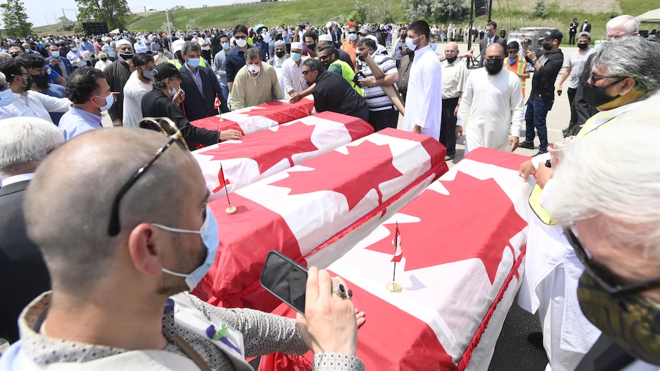 Quatre cercueils couverts de drapeaux canadiens sont encerclés par une foule