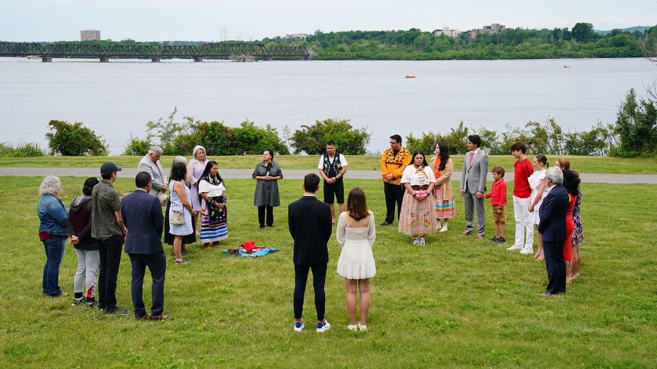 Debout, des dignitaires canadiens forment un cercle sur le bord de la rivière des Outaouais.