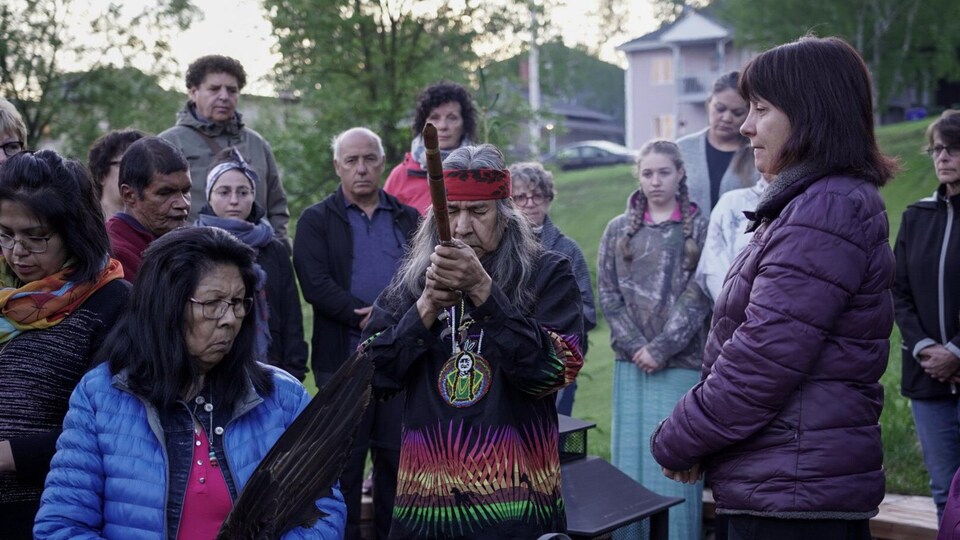 Un homme tient une pipe traditionnelle au sein de gens recueillis.