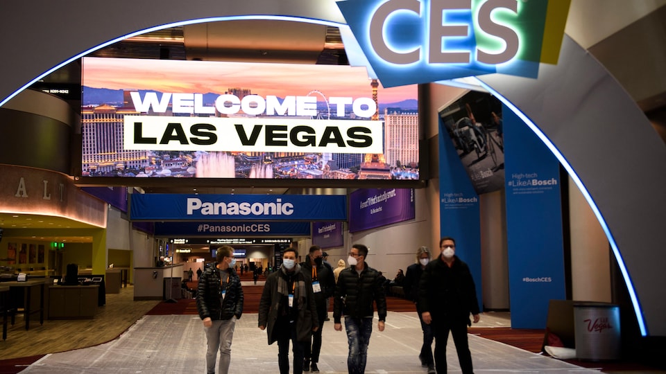Un groupe de personnes portant des masques chirurgicaux circulent dans un centre arborant les lettres «CES» et la mention «Welcome to Las Vegas». 