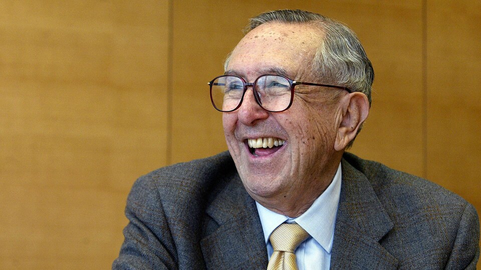 De profil, un homme portant des lunettes sourit à pleines dents.