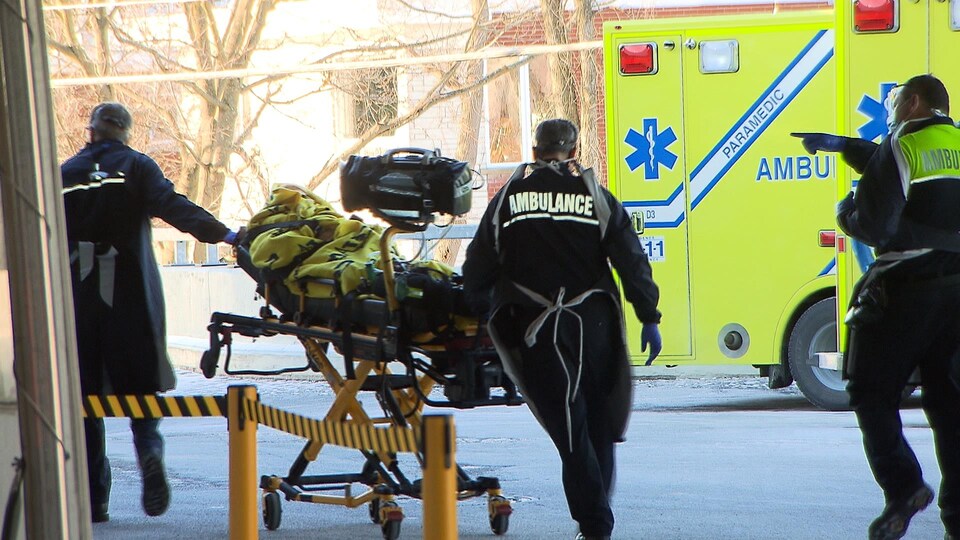 Des ambulanciers déplacent une personne sur une civière.