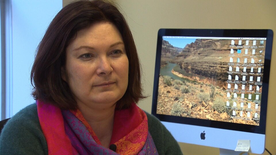 Une femme, assise devant un ordinateur, regarde une journaliste lors d'une entrevue dans son bureau.