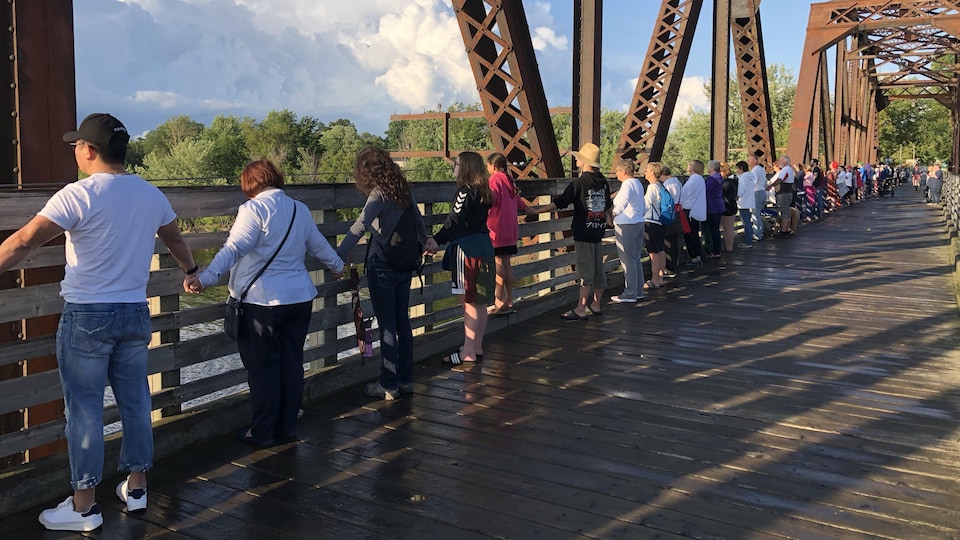Des gens se tiennent par la main le long d'un pont.