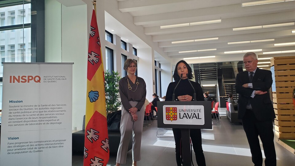 Ève Dubé devant un lutrin en conférence de presse avec les deux autres personnes à ses côtés.