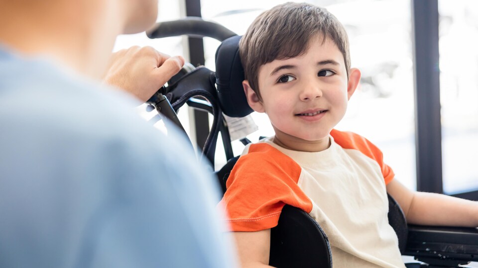 Un garçon en fauteuil roulant souriant et regardant avec admiration un thérapeute .