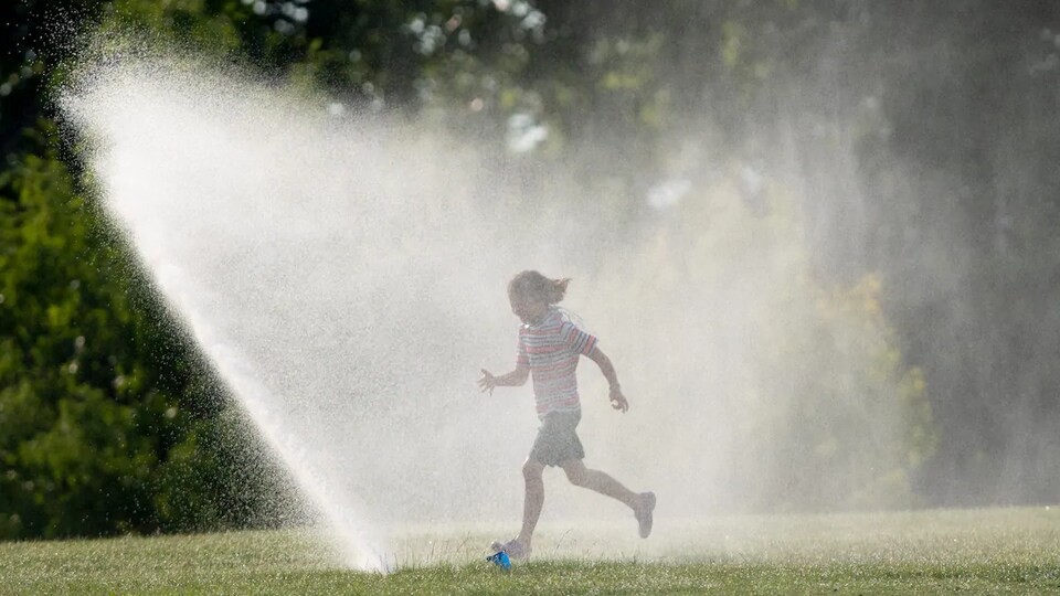 La jeune fille court sous un jet d'eau dans un parc.