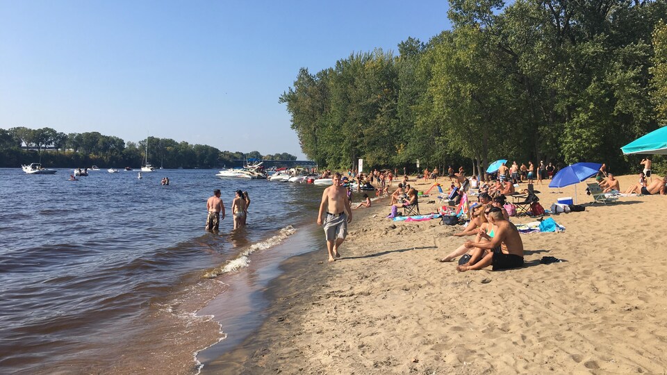 Plusieurs personnes sont installées sur la plage, certaines avec des parasols.
