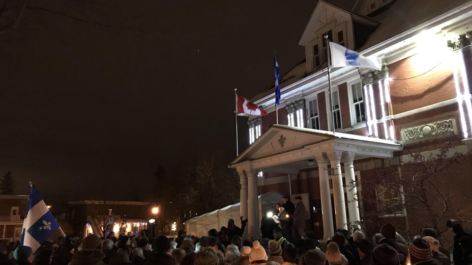 Des gens rassemblés à la nuit tombée, devant un bâtiment municipal