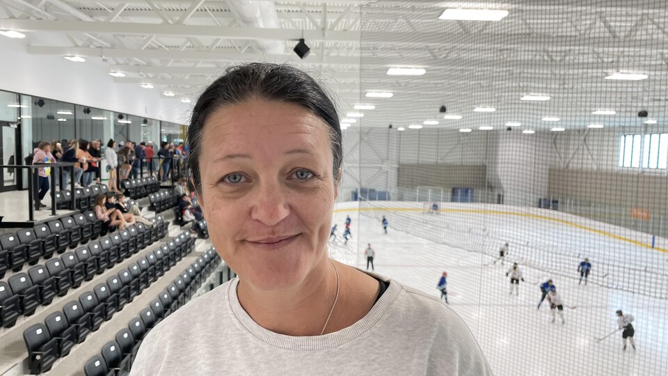 Portrait de Chantale Thibeault devant une patinoire sur laquelle se déroule un match de hockey féminin.