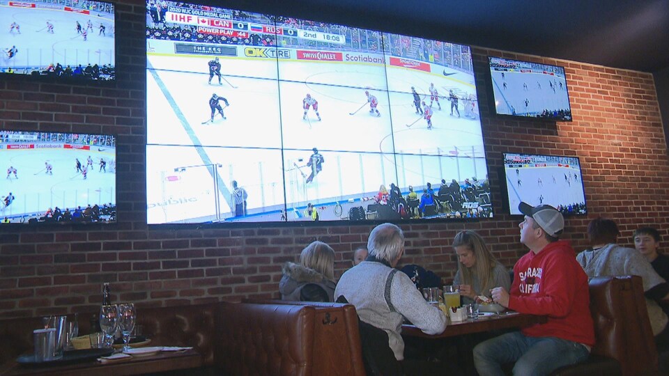 Des gens dans un restaurant avec un match de hockey diffusé sur écran géant.