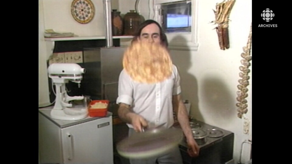 Dans une cuisine, un homme fait sauter une crêpe au dessus d'une poêle. 