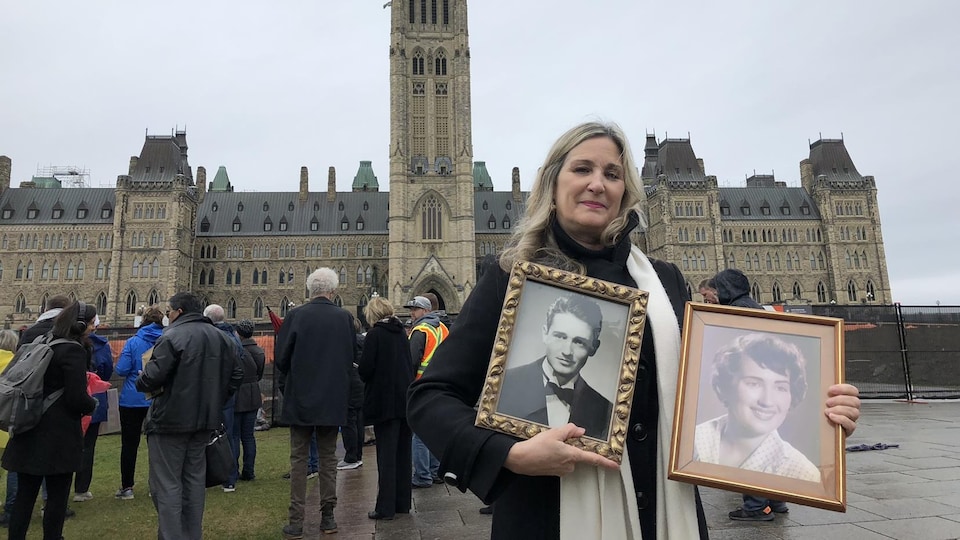 Chantal Jacob devant le Parlement à Ottawa avec des photos encadrées de ses parents. 