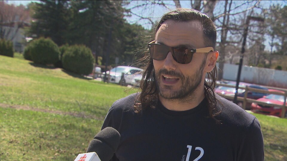 Un homme avec une barbe et des lunettes fumées parle au micro.