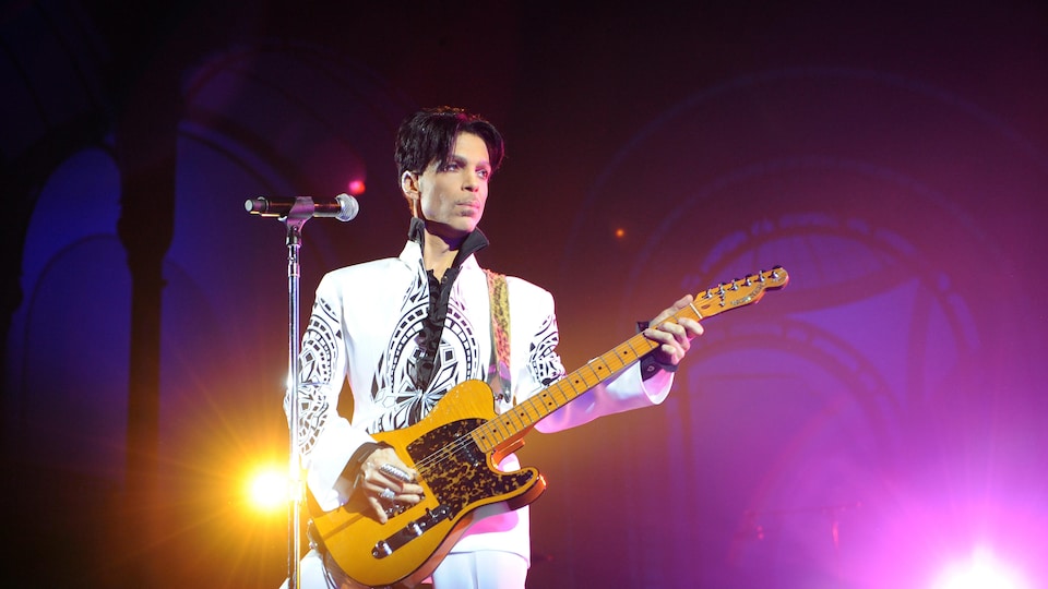 Le chanteur Prince joue de la guitare sur scène devant un microphone lors d'un concert à Paris, en 2009.