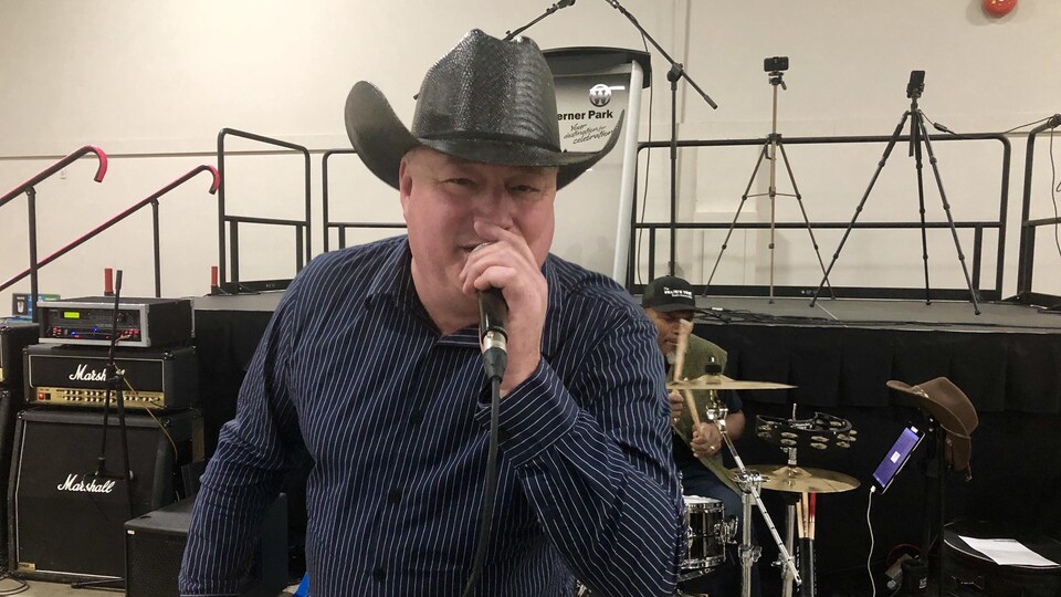 Un chanteur avec un chapeau de cow-boy chante, un micro à la main. 