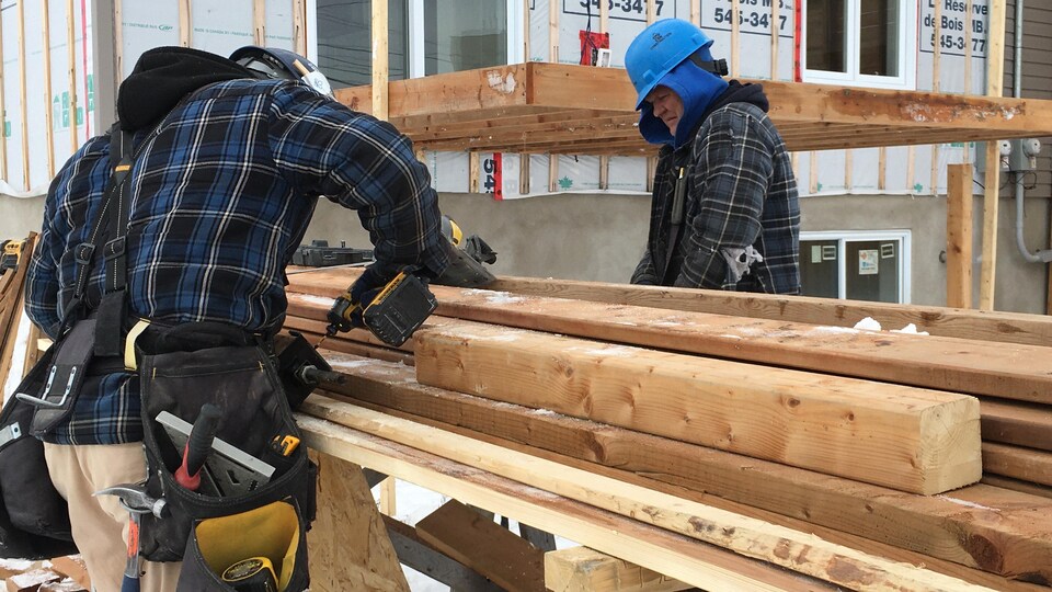 Des travailleurs préparent des planches près d'une maison en construction.