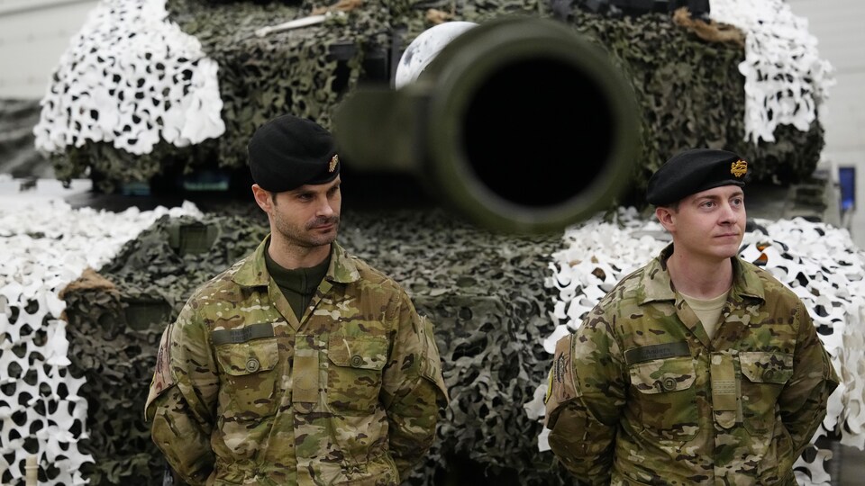 Deux soldats en uniforme devant le canon d'un char militaire.