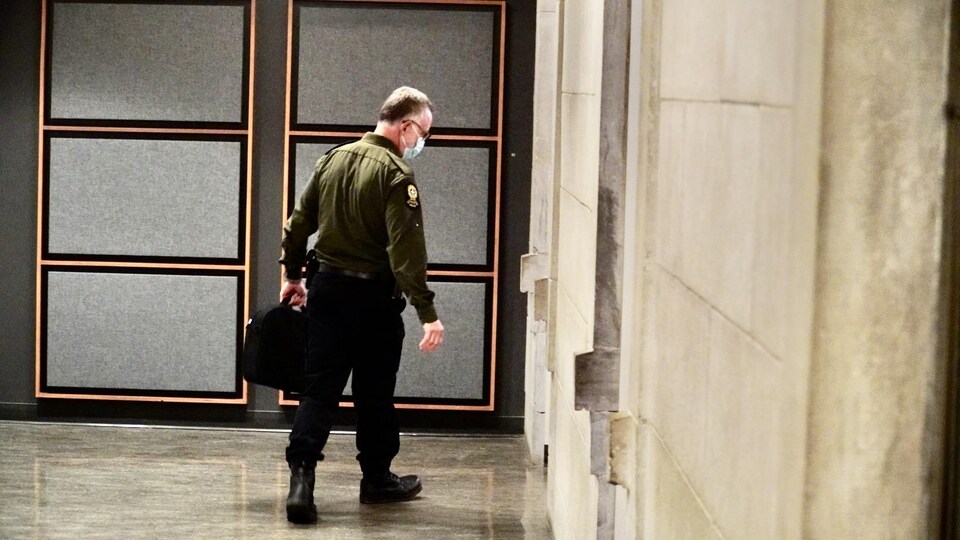 Charles Camiré qui marche vers la porte de la salle de cour avec un masque et un sac à la main.