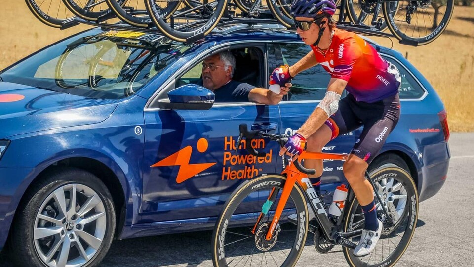 Charles-Étienne Chrétien, tout en roulant, se fait donner une nouvelle bouteille d'eau par son entraîneur qui est au volant de la voiture de l'équipe.