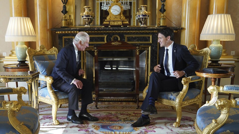 Charles III et Justin Trudeau assis face à face, discutent devant un foyer. 