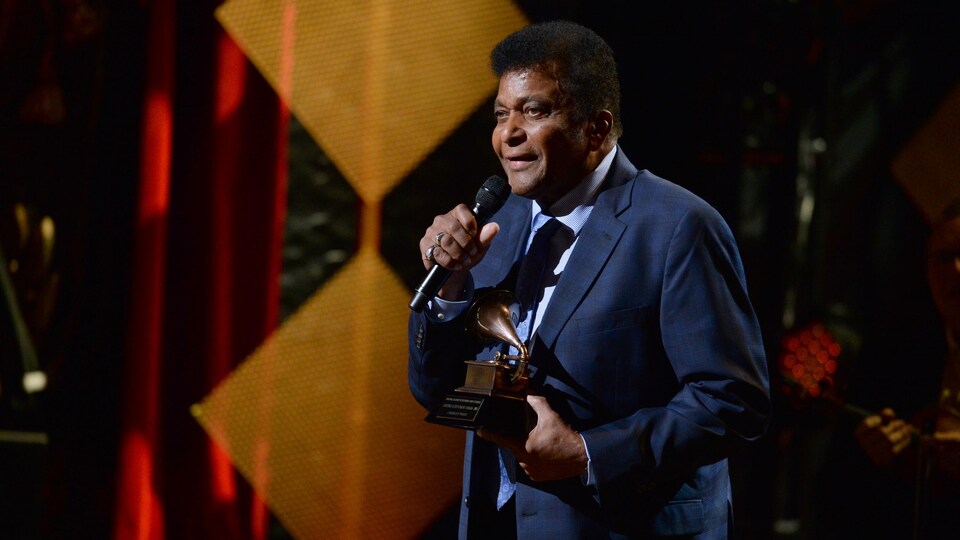 Un homme tient un trophée et parle dans un micro sur scène.