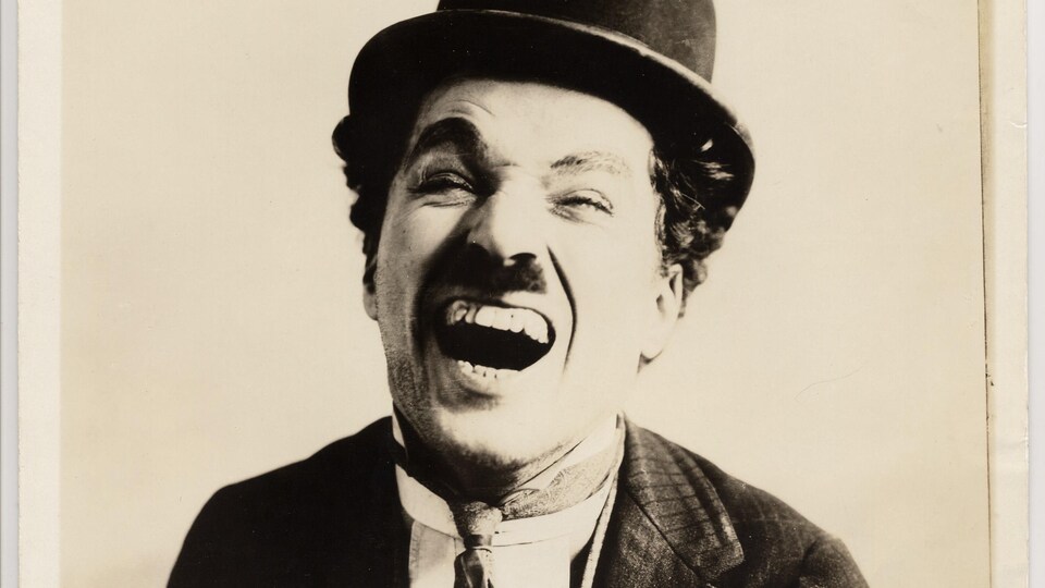 Photo en noir et blanc d'un homme portant un chapeau melon qui éclate de rire. 
