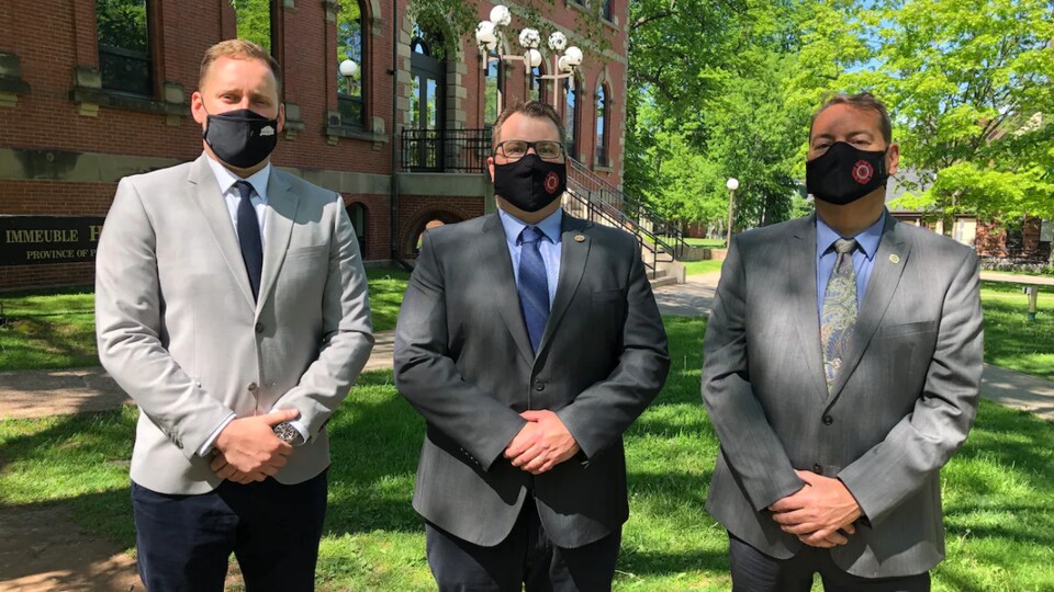 Les trois hommes devant l'édifice de l'Assemblée législative.