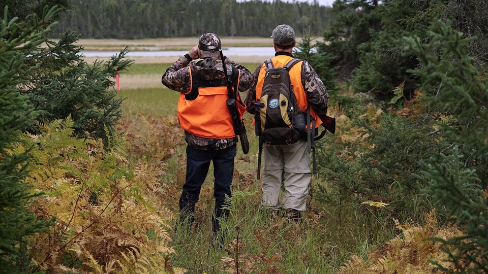 Deux chasseurs à l'orée d'un bois observent une étendue ouverte.               