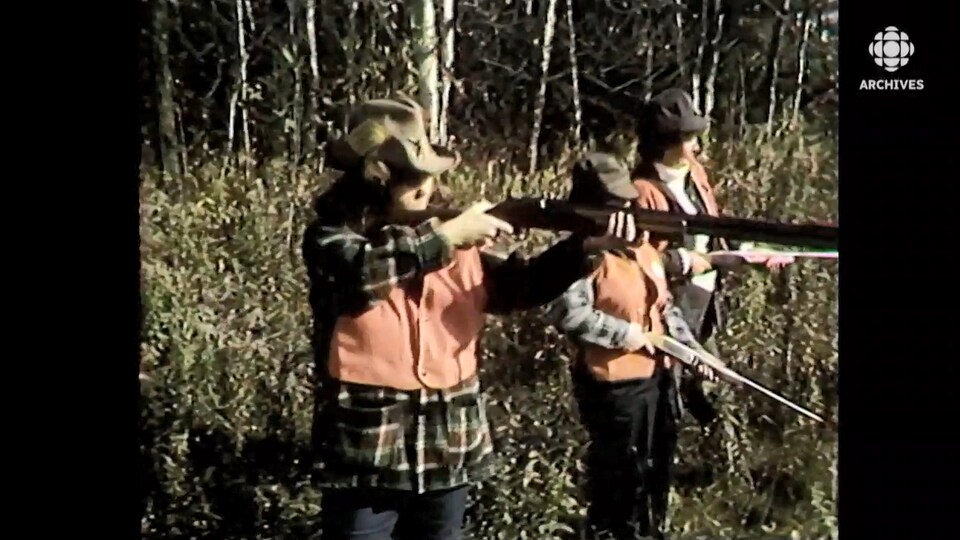 Trois femmes vêtues de dossards orange tirent au fusil dans une forêt.