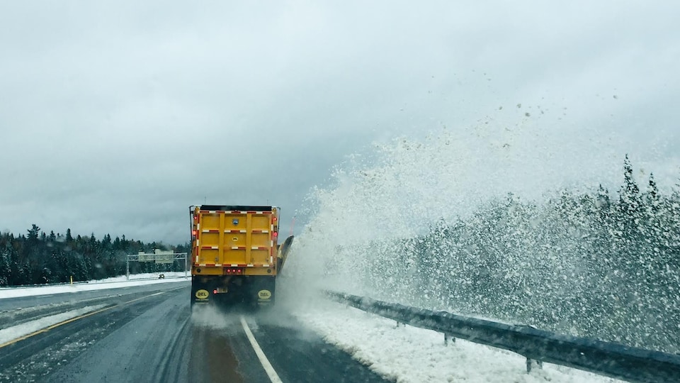 Un chasse-neige dégage une autoroute en projetant une gerbe de neige dans le fossé.