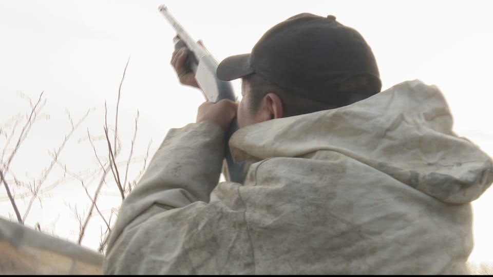 Un chasseur autochtone pointe des oiseaux migrateurs avec son fusil de chasse.