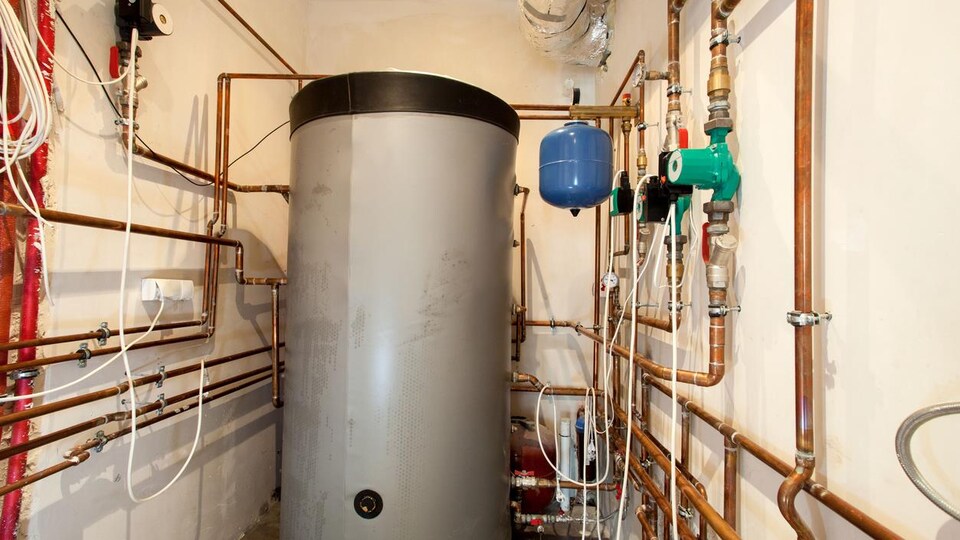 Un chauffe-eau dans un sous-sol, entouré de plusieurs tuyaux.