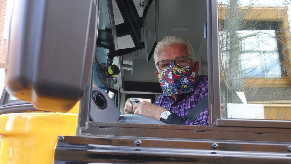 Un chauffeur porte un masque de tissu et des lunettes au volant de son autobus scolaire.
