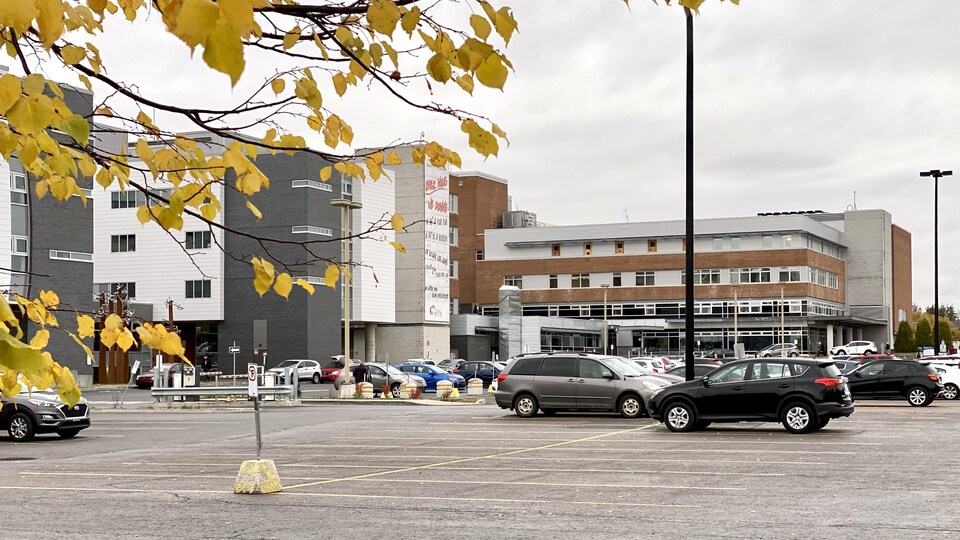 Extérieur de l'hôpital avec des voitures stationnées.