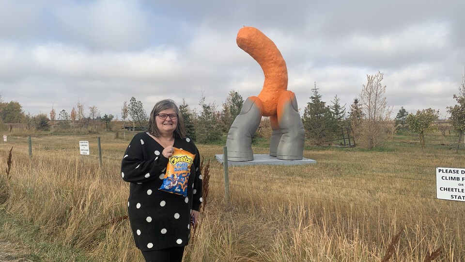 Cathie Pearson un sac de Cheetos à la main devant la sculpture Cheetle Hand.