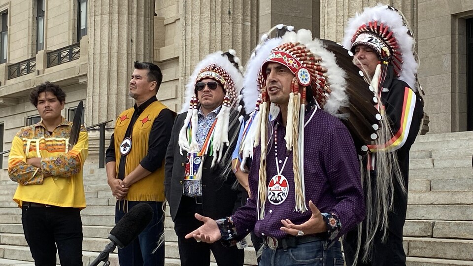 Cinq hommes réunis sur les marches du Palais législatif du Manitoba et le grand chef Dumas parle dans un micro.