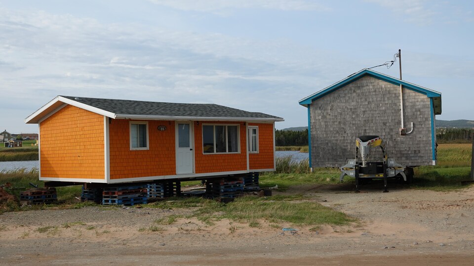 Un chalet orange est posé sur pilotis et un chalet gris est installé sur une remorque.